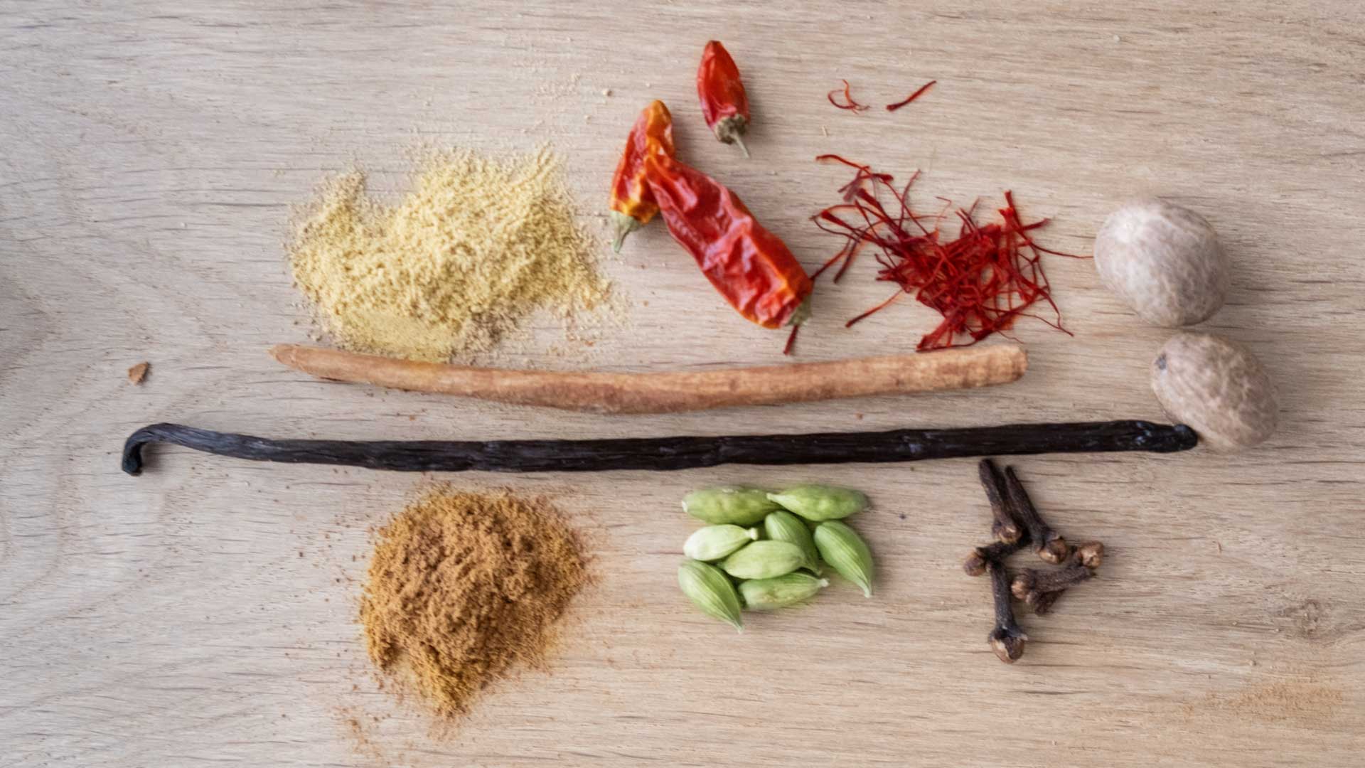 Hochwertige Gewürze wie Vanille und Kardamom auf Holz.