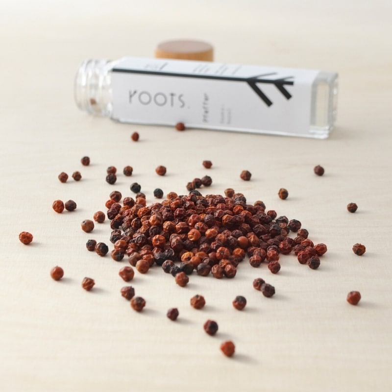 Roter Pfeffer von roots. Roter Pfeffer der Gattung Piper Nigrum verstreut vor dem roots. Gewuerzglas